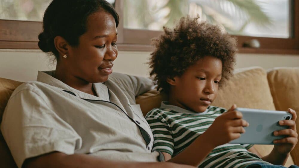 A parent and pre-teen child sitting on a couch looking at a smartphone and talking calmly