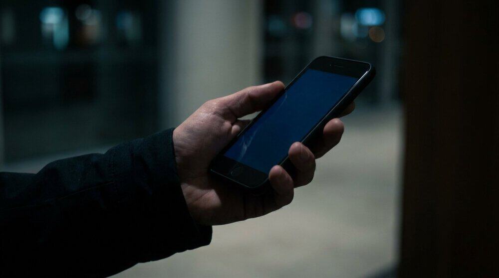 Hand holding smartphone with dark blue surveillance glow