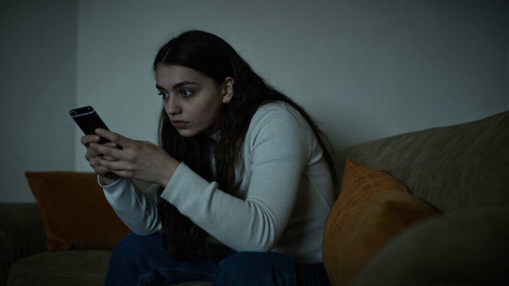 Worried woman looking at her smartphone at night