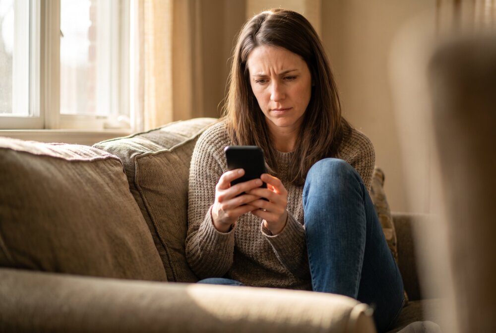 Worried woman checking her smartphone after it lost signal, a possible sign of SIM cloning